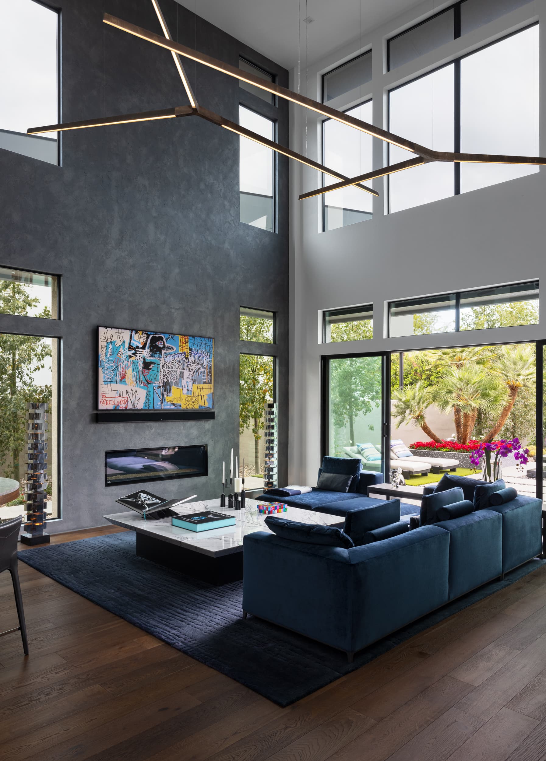 Two-story living room with blue velvet sectional and Basquiat-style art